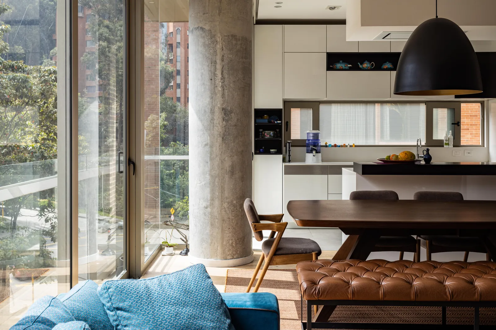 Estar y comedor con columna de hormigón, ventanal y cocina al fondo